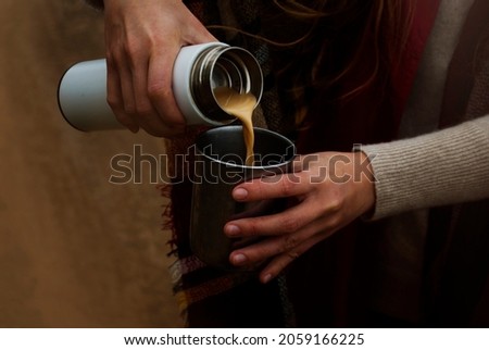 Pour from a thermos. Woman pours coffee with milk into a cup. Tourism and travel. Autumn photos. 