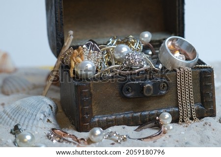 View of a miniature figure that is grasping a pearl on an old treasure chest on light sand and full of jewelry