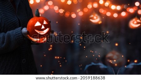 Jack o lantern glowing with moonlight in night forest. Halloween bokeh background with burning orange pumpkin that a men holds in his hands. Happy Halloween banner. Copy space for text