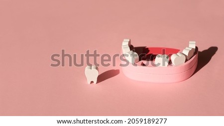 Wooden model toy of a human jaw with a missing tooth on a pink studio background. The problem of tooth loss. Baby milk teeth. Banner. Copy space.  Royalty-Free Stock Photo #2059189277