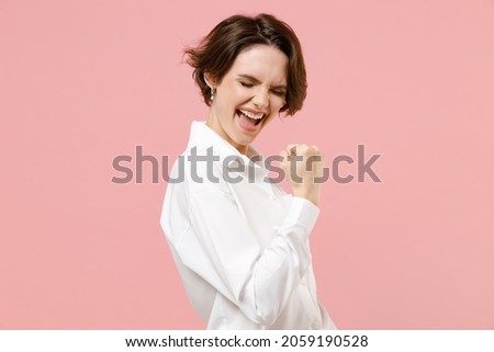 Young fun overjoyed successful employee business woman corporate lawyer 20s in classic formal white shirt work in office do winner gesture clench fist say yes isolated on pastel pink background studio Royalty-Free Stock Photo #2059190528