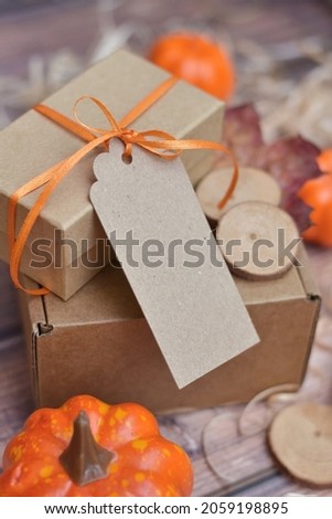 craft label, gift box is tied with an orange ribbon and pumpkins, wooden background. happy halloween, thanksgiving day, eco friendly packaging. zero waste. harvest. fall shopping sale