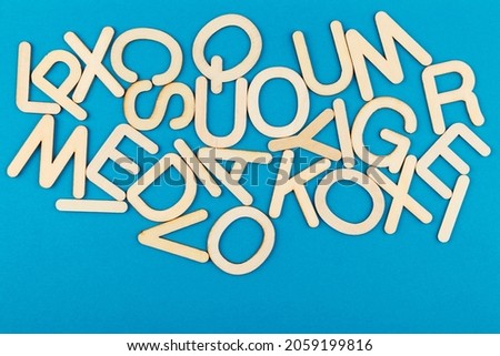 Wooden alphabet letters on blue paper background. A lot of wooden letters with copy space. Chaos concept.