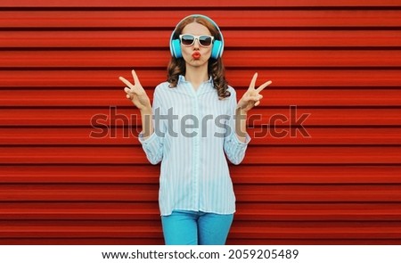 Portrait of young woman with headphones listening to music on a colorful red background