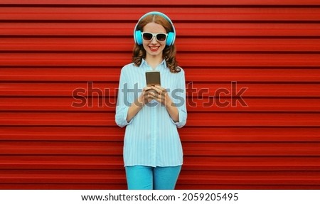 Portrait of smiling young woman in headphones listening to music with smartphone on red background