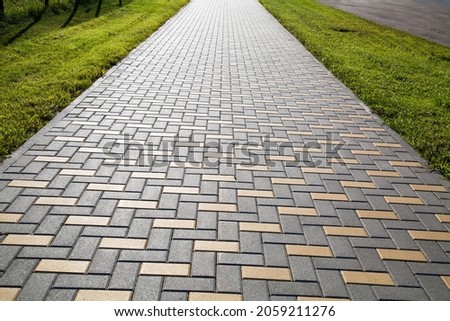 A sidewalk made of rectangular artificial stone extending into the distance in yellow and gray with a green lawn, texture backgrounds for graphic design. Abstract wallpaper. Royalty-Free Stock Photo #2059211276