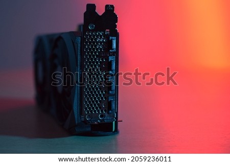 Black graphics card with two fans (rear photo), on a wooden table, with red and blue lighting. Royalty-Free Stock Photo #2059236011
