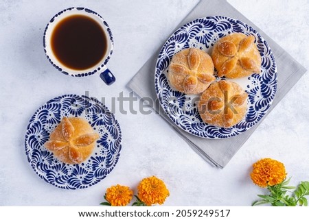 Traditional Mexican bread of the dead also known as "Pan de Muerto" on traditional Mexican tableware and orange flowers known as cempasuchil on white textured background.