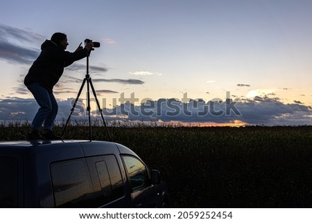 The girl on the roof of the car photographs the sunset with a tripod.