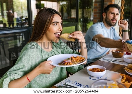 young latin woman eating mexican tacos on a restaurant terrace in Mexico Latin America, feeling happy on a summer day