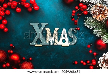 Blue Christmas or New Year background with red Christmas balls, berries, fir branches, pine cones and inscription Xmas, top view