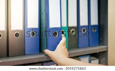 Female hand holding a binder of documents on the row of file folders that nicely management system on the office's shelves. Royalty-Free Stock Photo #2059275863