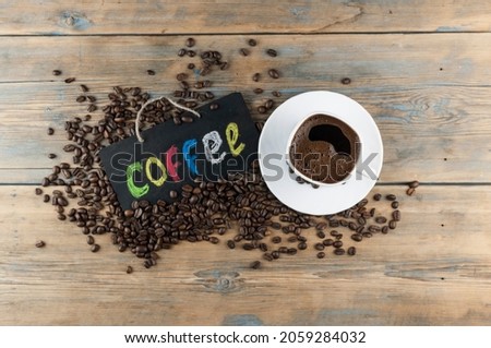 White ceramic cup of coffee and blackboard with inscription "coffee" writen colorful alphabet. Coffee break, morning awakening concept. Top view