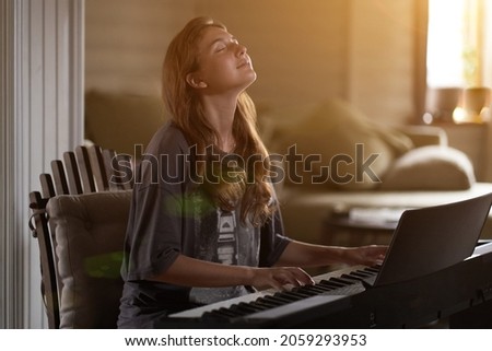 A young woman playing the piano.Close-up of a beautiful blonde girl with reddish-brown hair playing the piano creative, performance, musical concept, she wearing a T-shirt and playing a black piano. Royalty-Free Stock Photo #2059293953