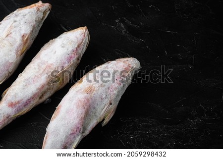 Frozen red mullet or barabulka raw fish set, on black dark stone table background, top view flat lay , with copy space for text