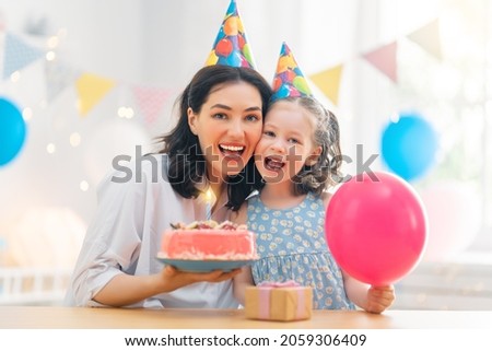The kid is blowing out the candles on the cake. Mother and daughter are celebrating birthday.