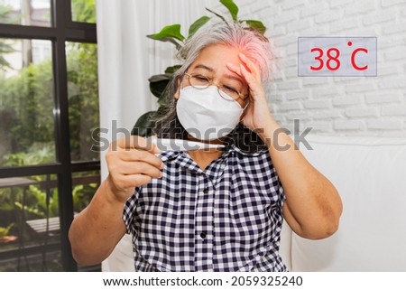 Asian-aged woman wearing a headache mask uses a digital thermometer to check her body temperature. High fever 38 degrees Celsius She is ill in the deadly situation of the Covid-19 pandemic.