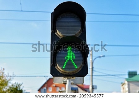 Small two-piece traffic light with green light on in front of the pedestrian crossing