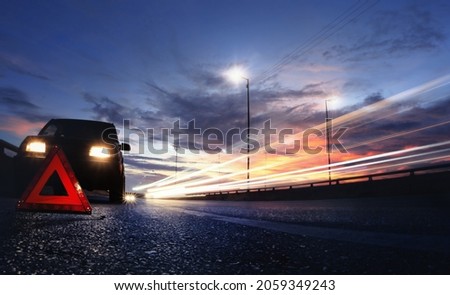 Red emergency stop sign (red triangle warning sign) in front of black SUV car  and beautiful sunset sky,long shutter speed exposure.