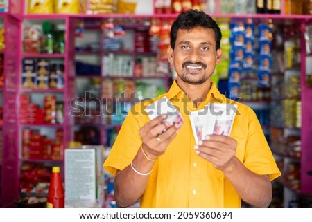 Happy smiling Groceries or Kirana Merchant small business owner Counting money by looking at camera - concept of Successful business, profit making, banking and finance. Royalty-Free Stock Photo #2059360694