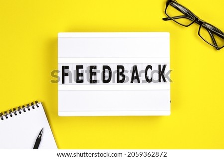 Feedback word on lightbox with eyeglases and notepad on yellow background, flat lay