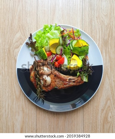Grilled pork chop steak with salad on the black and white plate. Wooden table. Keto, ketogenic, Atkins diet recipe. Low carb, high fat. Avocado is good fat. Fresh vegetables. Diabetes patients' food. Royalty-Free Stock Photo #2059384928
