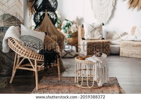 Comfortable living room with ethnic interior design in bohemian style. Apartment with home decor, rattan furniture, armchair with cushions, bamboo coffee table, carpet on wooden floor Royalty-Free Stock Photo #2059388372