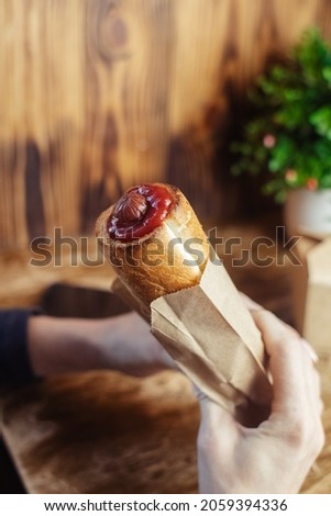 Close-up of a hot dog in hand. The girl has a French manicure. There is a lot of ketchup on top and sauce on the food. The woman wrapped her hands around the bun, creating a hint of intimacy.