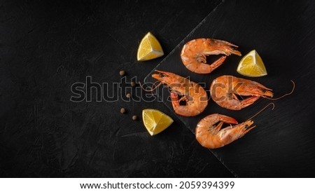 boiled shrimps lie on a stone board on a black concrete surface with lemon wedges and peas. top view. artistic dark photo with copy space