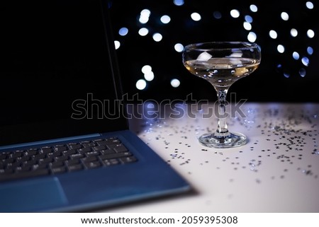 Glass of champagne and laptop on light bokeh background, celebration and work, close-up.