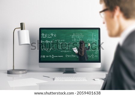 Young businessman at office desk looking at computer screen with online education chalkboard and formulas pattern. Digital knowledge and webinar concept