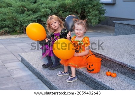 A little girls in a Halloween costume is sitting with balls in hands outdoors