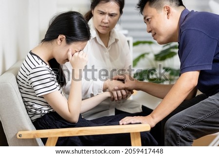 Asian parents give advice,talk sharing thoughts care to teenage girl,mom and dad holding hands to comfort and consoling daughter together,sad teenager student crying at home,family life relationship Royalty-Free Stock Photo #2059417448