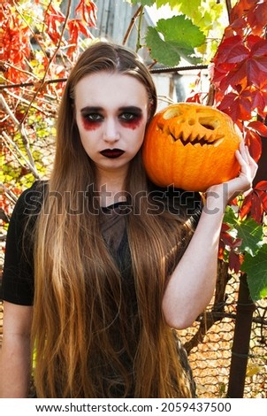 Halloween. A beautiful woman in the image of a witch holds a pumpkin monster, jack lantern on a background of autumn nature.
