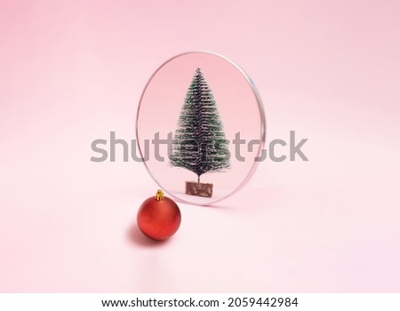 Red Christmas bauble look in to mirror and see new year green snow tree. Pink pastel background. Minimal holiday design and concept.