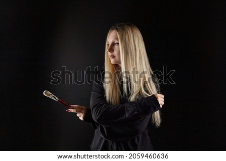 young blonde artist poses with a brush in her hand. photo shoot on a black background in the studio.