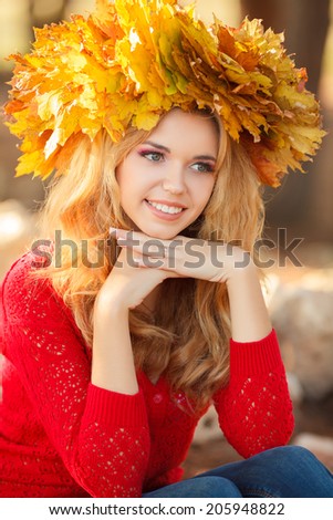 Young woman with autumn leaves in hand and fall yellow maple garden background. Woman with wreath of yellow leaves on head. Autumn bright portrait. 
