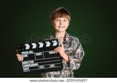 Little girl in military uniform and with movie clapper on dark background