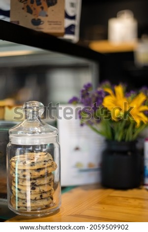 Food, dessert, baking and lifestyle concept - Close-up of a glass jar with chocolate chip cookies against a composition of wild flowers in a clear vase in a coffee shop with space for copying
