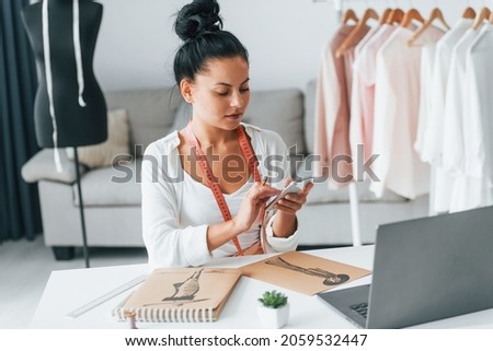 With laptop. Seamstress is in her office that is with different clothes.