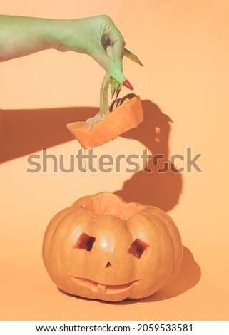 A scary witch holds a pumpkin handle on an orange background. Minimal layout