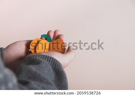 Little child holding pumpkin made from paper. Halloween holiday concept, Thanksgiving day or autumn handmade decor. Copy space, close up