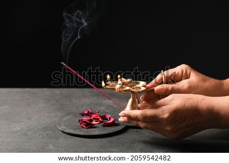 Female hands with diya lamp and aroma stick for celebration of Divaly on dark background