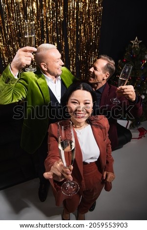 High angle view of asian woman holding champagne near friends and christmas tree on black background