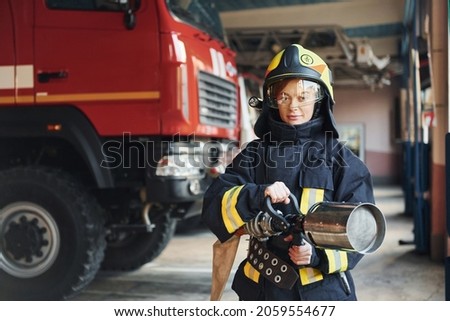 Hose in hands. Female firefighter in protective uniform standing near truck.