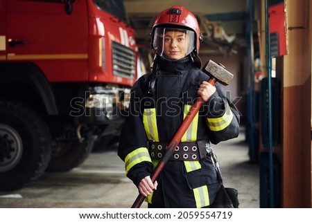 With hammer in hands. Female firefighter in protective uniform standing near truck.