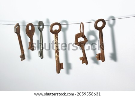 A different old retro rusty keys from different locks hanging on string with a drop shadow on a white wall