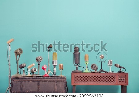 Retro classic microphones for press conference or interview on wooden TV stand and old case front mint blue background. Vintage style filtered photo