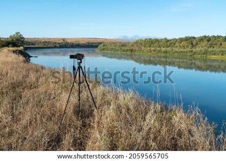 a camera on a tripod taking pictures of nature installed on the river bank