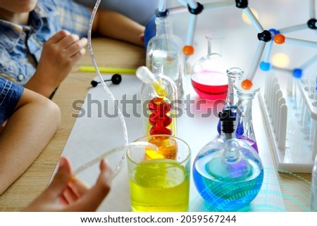 two children 7-9 years old, elementary school boys, do chemical experiments, pour colored liquids into glass flasks, mix colors, school education concept, hands-on study of chemistry